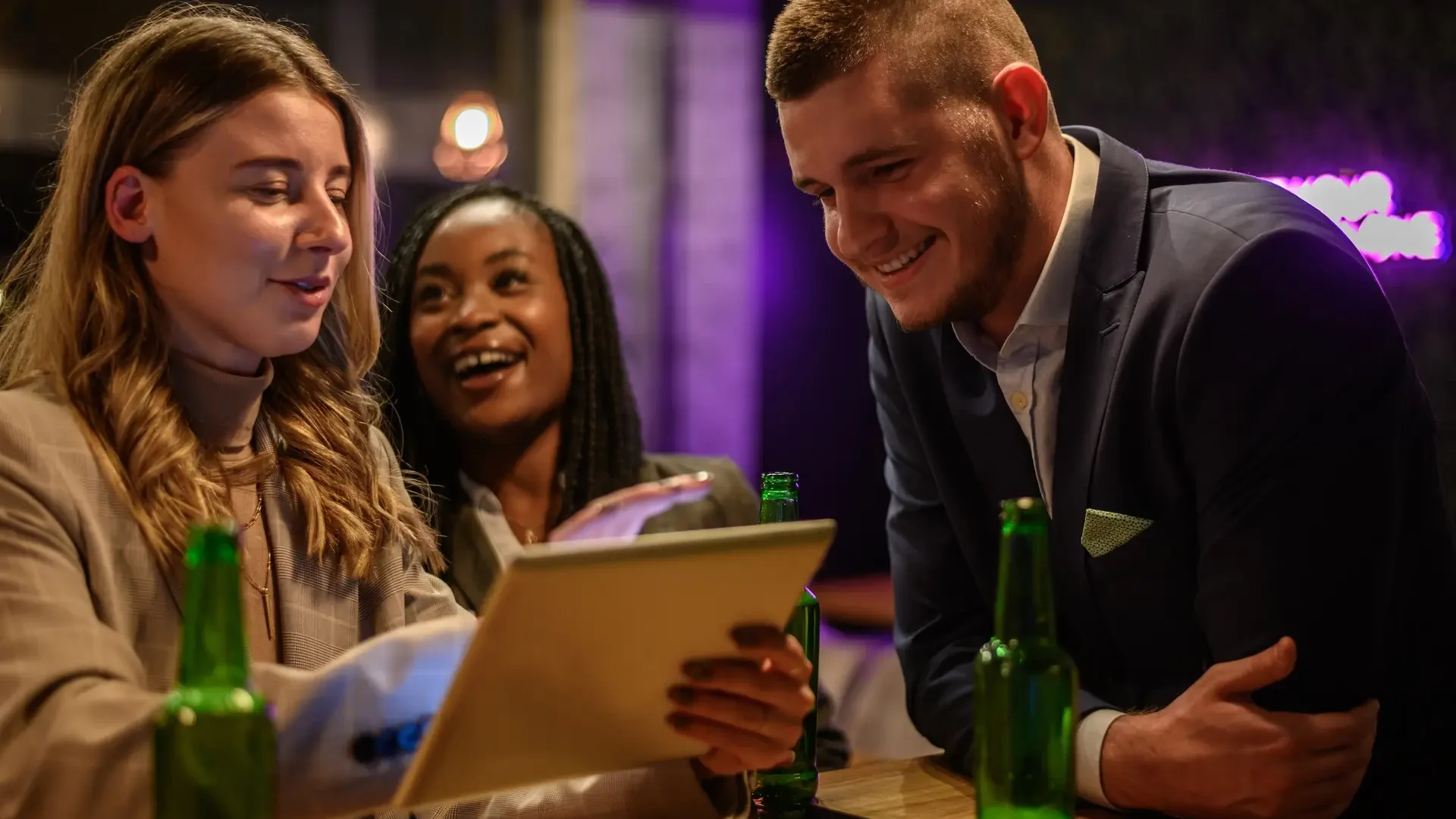 Cheerful colleagues drinking beer in the bar together after work and using a tablet